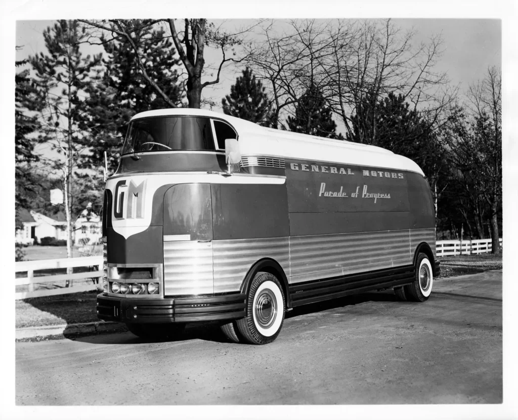 Futurliner первого поколения с прозрачным колпаком над кабиной, буквами GM на носу и надписью General Motors Parade of Progress на борту стоит у дороги среди деревьев