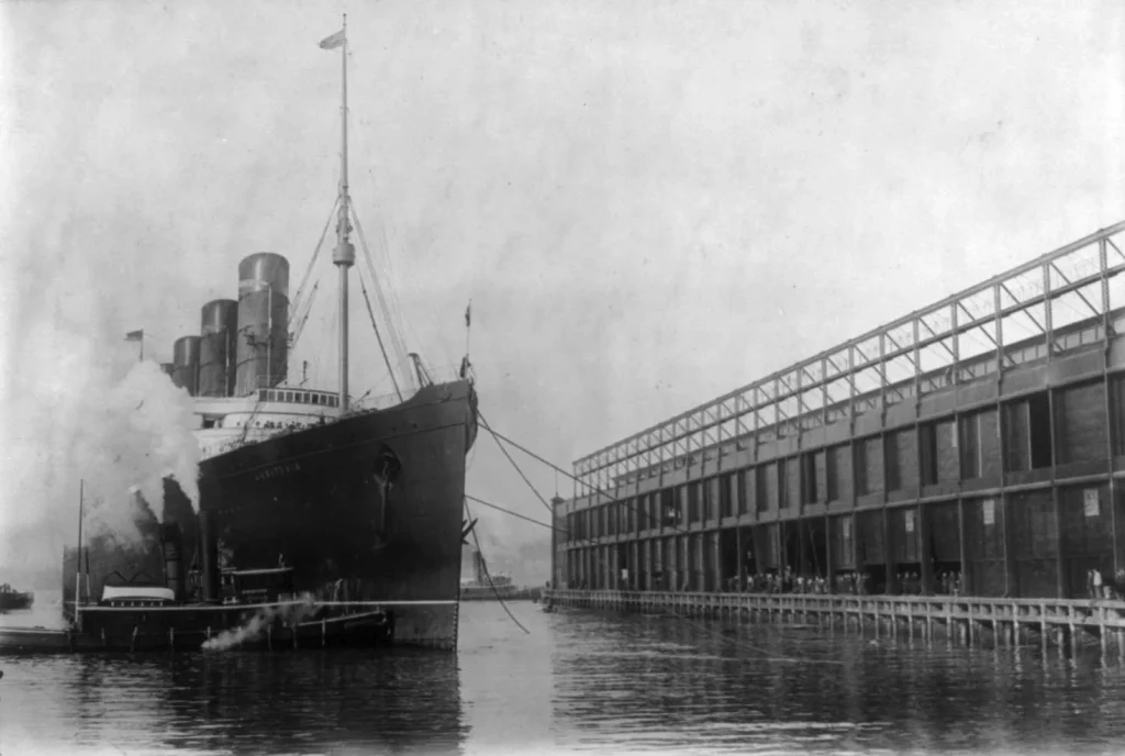 Нос «Лузитании» у нового пирса Cunard на Гудзоне в Нью-Йорке, рядом буксир в клубах пара, 20 ноября 1908 года