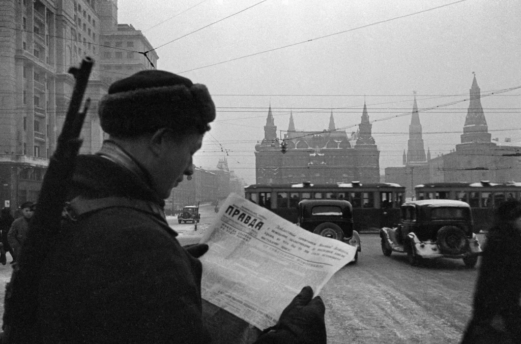 Боец с винтовкой читает газету «Правда» на улице Москвы, ноябрь 1941 года, вдали Исторический музей