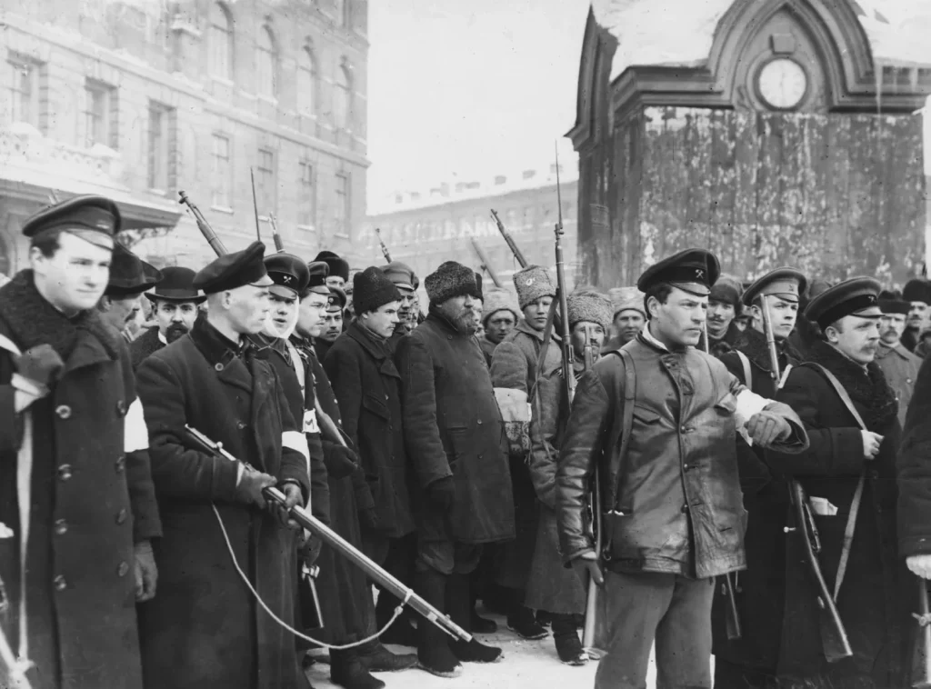 Вооружённый патруль с белыми повязками на рукавах ведёт задержанных по улице