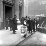 Мальчик-газетчик в кепке держит плакат «Titanic disaster great loss of life — Evening News» у входа в контору White Star Line в Лондоне, рядом мужчины в котелках читают газеты