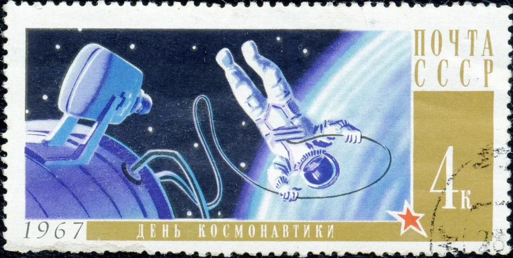 Почтовая марка СССР 1967 года «День космонавтики»: космонавт на фале у шлюза корабля над Землёй